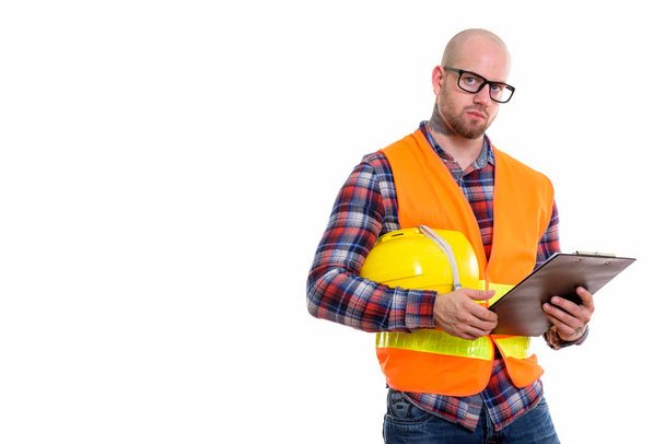 Bald muscular man construction worker holding safety helmet and clipboard - 写真・画像