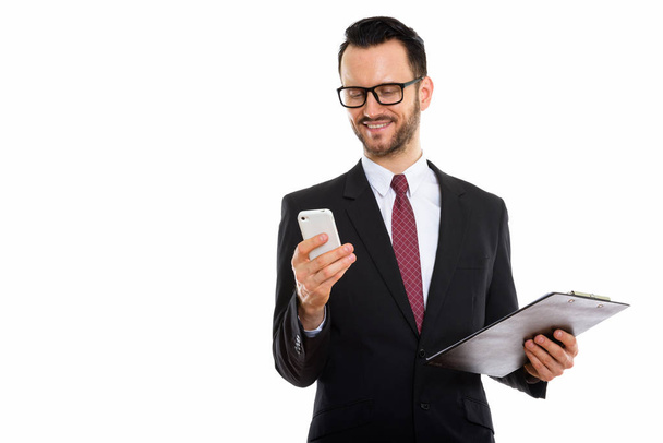 Студійний знімок молодого щасливого бізнесмена, який посміхається і тримає кишеню під час використання мобільного телефону
 - Фото, зображення