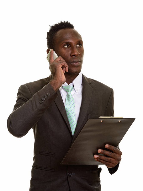 Pensativo joven empresario africano negro hablando por teléfono móvil mientras sostiene el portapapeles - Foto, imagen