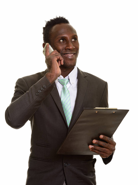 Zamyšlený mladý šťastný africký podnikatel s úsměvem a mluvení na mobilním telefonu při držení schránky - Fotografie, Obrázek