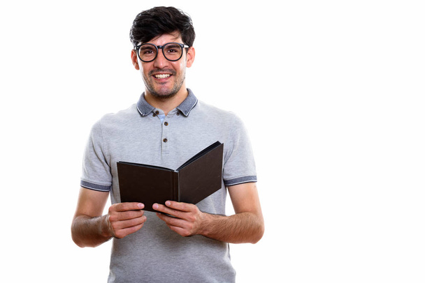Studio shot of young happy Persian man smiling while holding book - 写真・画像