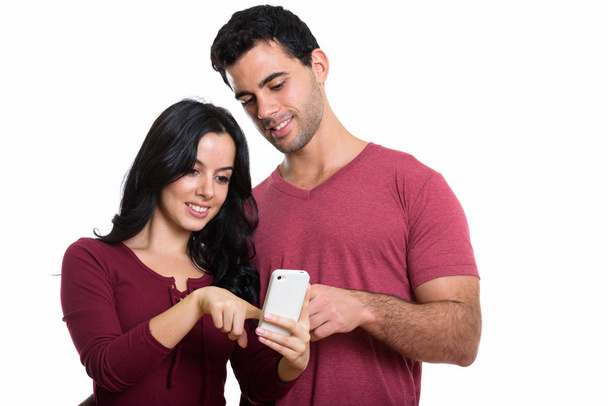 Studio shot of young happy couple smiling while using one mobile phone together - Φωτογραφία, εικόνα