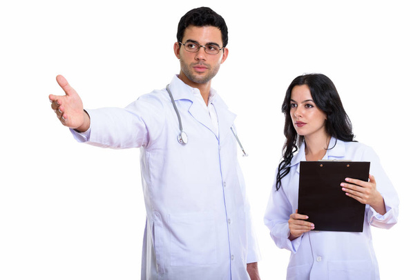 Στούντιο πλάνο του νεαρού άνδρα γιατρό δείχνει κάτι και γυναίκα γιατρός κρατώντας πρόχειρο - Φωτογραφία, εικόνα
