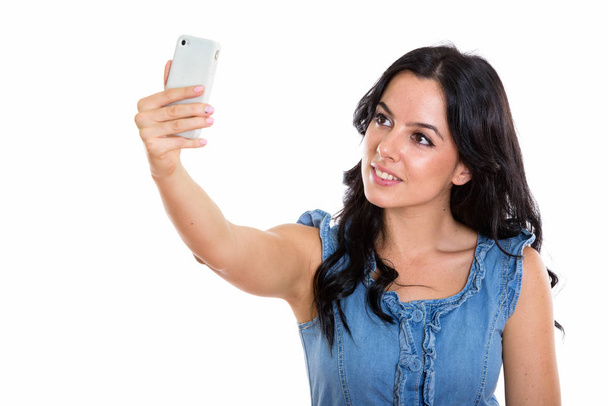 Studio laukaus nuori onnellinen espanjalainen nainen hymyilee ottaessaan selfie kuva matkapuhelimella - Valokuva, kuva