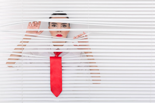 Portret van een vrouw op zoek via de blinds - Foto, afbeelding