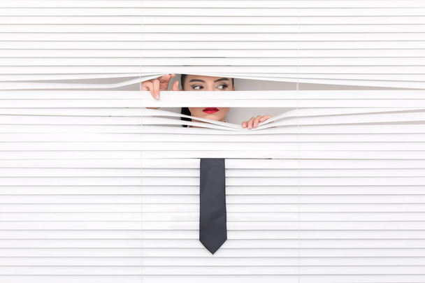 Portrait of a woman looking through out the blinds - 写真・画像