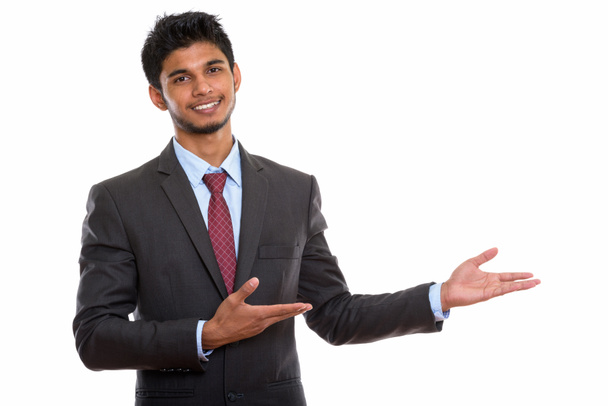 Студийный кадр молодого счастливого индийского бизнесмена, улыбающегося, показывая что-то - Фото, изображение
