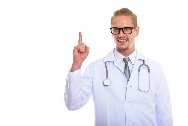 Студійний знімок молодого щасливого лікаря, який посміхається, вказуючи пальцем вгору
 - Фото, зображення