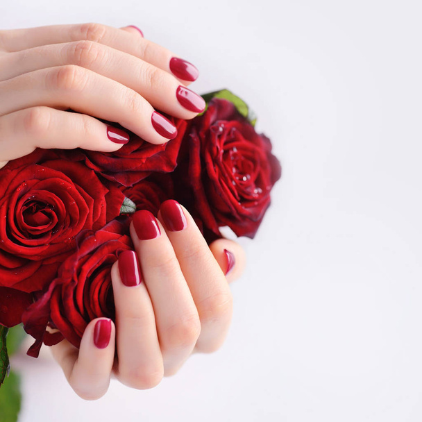 Mãos de uma mulher com manicure vermelho escuro com um buquê de rosas vermelhas
 - Foto, Imagem