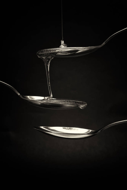 Honey pouring from spoon against a dark background - 写真・画像