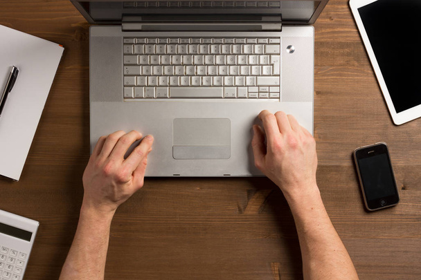 Деревянный рабочий стол с руками человека и ноутбуком на работе
 - Фото, изображение