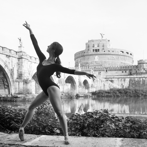 Young beautiful ballerina dancing out in Tevere riverside with castel Santangelo in the background in Rome, Italy. Black and white image. Ballerina Project. - Fotó, kép