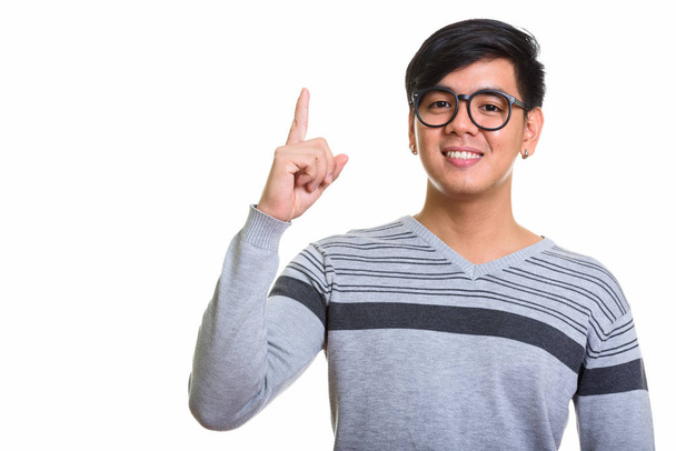 Studioaufnahme eines glücklichen asiatischen Mannes, der lächelt und mit dem Finger nach oben zeigt - Foto, Bild