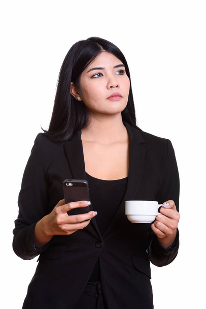 Thoughtful young Asian businesswoman holding mobile phone and co - Photo, Image