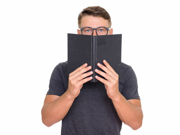 Studio shot of young handsome Caucasian man hiding behind book i - Photo, image