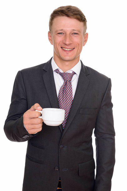 Studio shot of young happy Caucasian businessman holding coffee  - Photo, Image