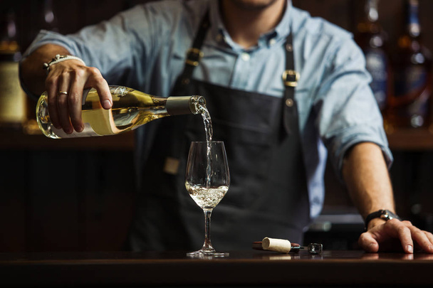 Male sommelier pouring white wine into long-stemmed wineglasses. - Foto, Imagen
