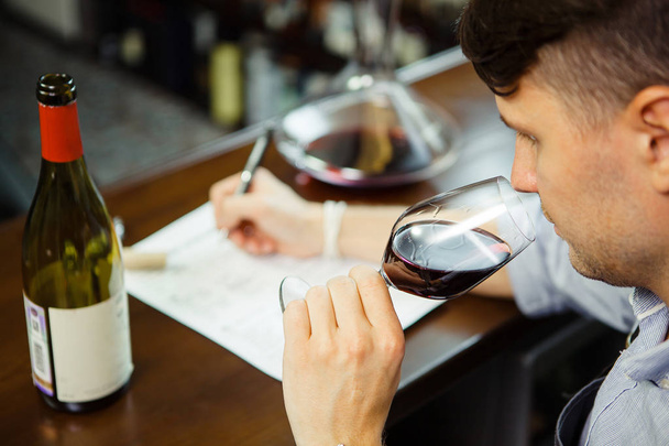 Male sommelier tasting red wine and making notes at bar counter - Foto, Bild