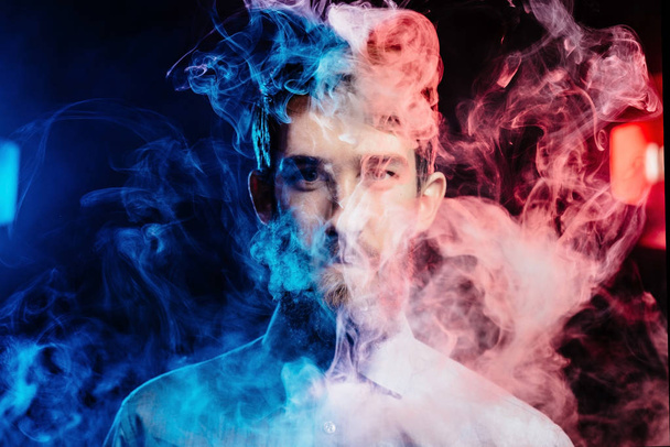 Young guy with a beard vaping and releases a cloud of vapor. hipster vaper smoke vaporizer. - Photo, image