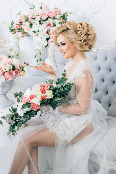 Kaunis blondi tyttö istuu sohvalla pukeutunut valkoinen aamutakki tilalla häät kukkakimppu, lähettämällä ilmapusu taustalla monia värejä
 - Valokuva, kuva