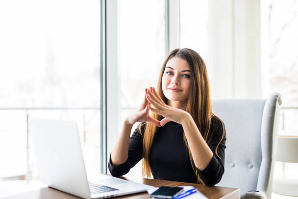 jovem mulher de negócios bonita trabalhando no laptop e mantendo a mão no queixo enquanto sentado em seu local de trabalho
 - Foto, Imagem