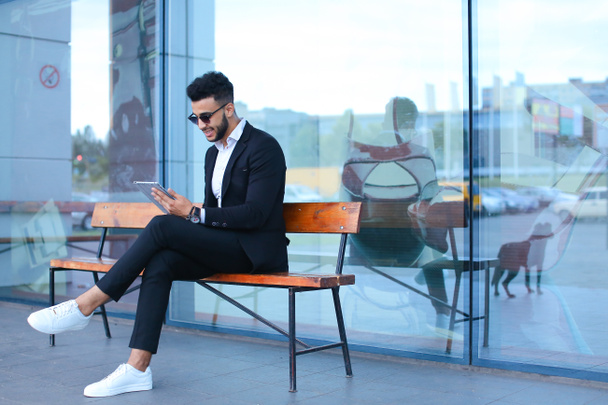 Man in suit arabic puts on sunglasses with tablet near business - Fotó, kép
