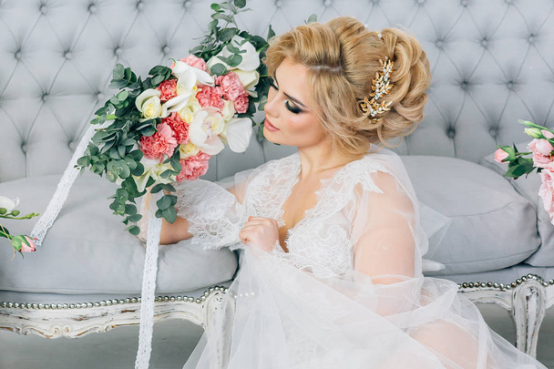 belle blonde en robe de chambre avec les cheveux et le maquillage tient un bouquet de mariage
 - Photo, image