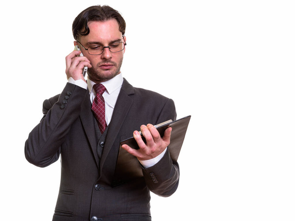 Studio shot of young businessman talking on mobile phone while r - Photo, Image
