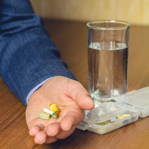 Copo de água, vitaminas e nutricionais, pílulas de suplemento dietético segurando na mão de homem de negócios no local de trabalho, close-up
 - Foto, Imagem
