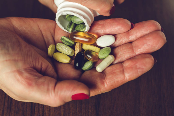 Vrouw handen schonk de mix van vitaminen en voedingssupplementen pillen uit een fles, close-up - Foto, afbeelding
