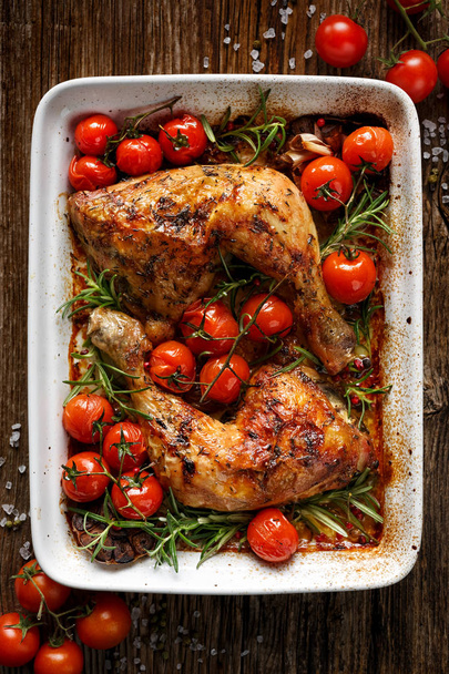 Quarto de frango assado com tomate cereja e alecrim em um prato de caçarola na mesa de madeira
 - Foto, Imagem