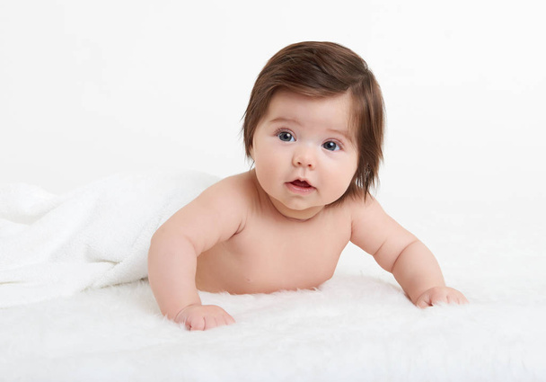 Adorablemente el bebé se acuesta sobre una toalla en la cama, fondo blanco. Feliz infancia y concepto de salud
 - Foto, Imagen