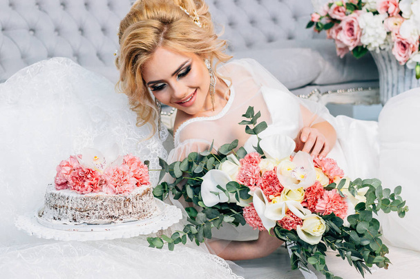 schöne Braut mit Hochzeitsfrisur und Make-up in der Nähe einer Torte mit einem Strauß in den Händen - Foto, Bild