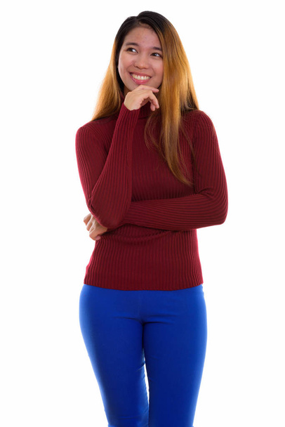 Studio shot of young happy Asian woman smiling while standing an - Foto, immagini