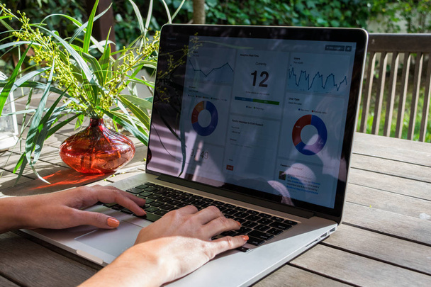 Женские руки с помощью ноутбука с аналитическим графиком на столе в саду, работа на свежем воздухе, фрилансер
 - Фото, изображение
