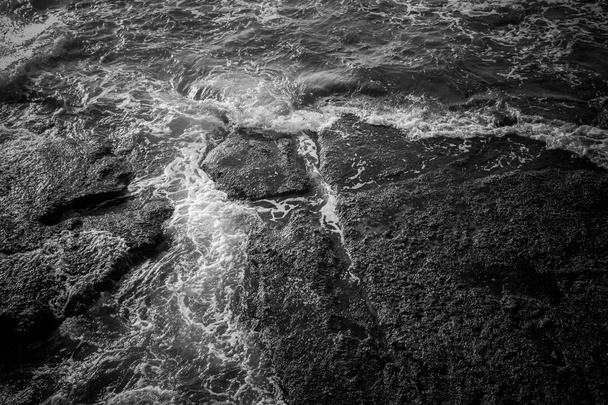 Witte Zee schuim en zwarte rotsen oppervlak - Foto, afbeelding