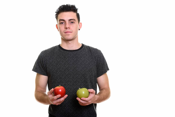 Studio shot of young man holding red and green apple - Фото, изображение
