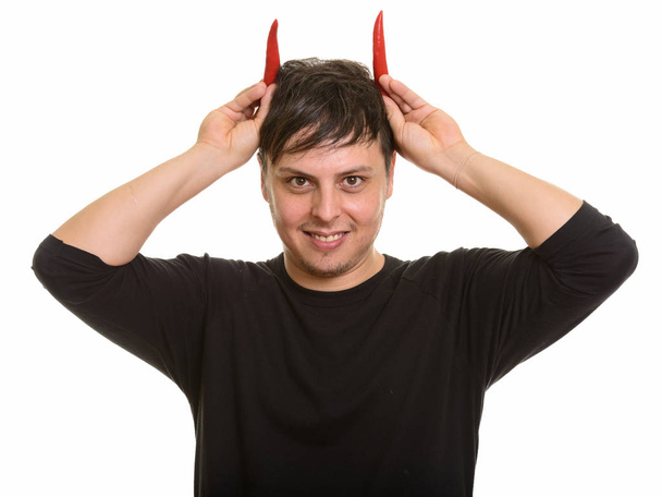 Studio shot of crazy Caucasian man with red peppers as horns smi - Fotoğraf, Görsel