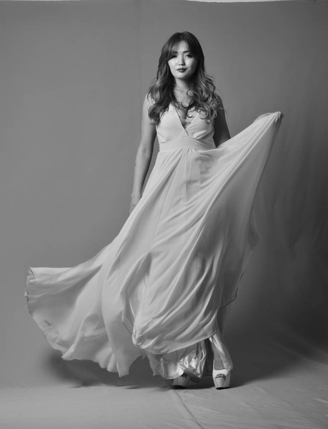 Молодая азиатская модель позирует в элегантном длинном платье, развевающемся на ветру
 - Фото, изображение