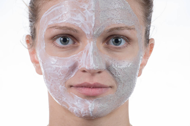 Two cosmetic mask of gray clay with scrub and cream on the face  - Photo, Image
