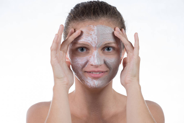 zwei kosmetische Maske aus grauem Ton mit Peeling und Creme auf dem Gesicht  - Foto, Bild