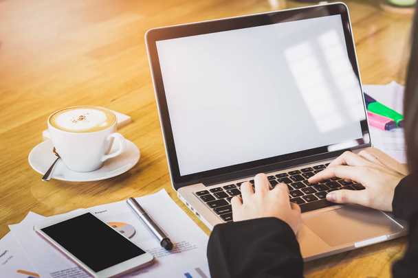 Weicher Fokus der weiblichen Hand, die mit Telefon und Laptop auf einem Holztisch im Büro im Morgenlicht arbeitet. Jahrgangseffekt - Foto, Bild