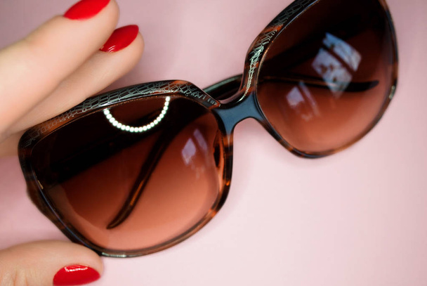 gafas de sol en la mano con uñas rojas
  - Foto, Imagen