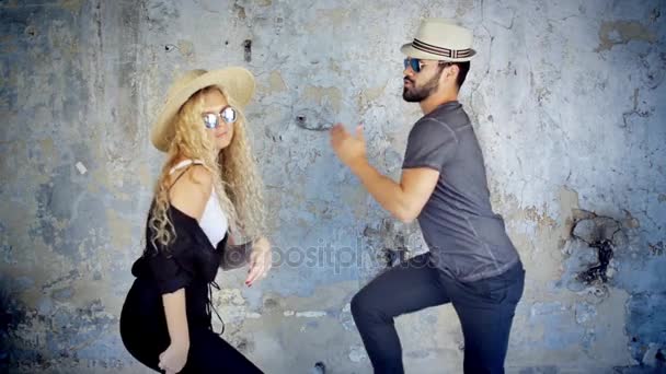 Feliz pareja joven en gafas de sol y sombreros bailando en cámara lenta escuchando música divirtiéndose en el amor
. - Imágenes, Vídeo