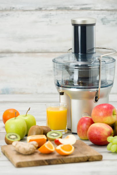 Modern electric juicer, various fruit and glass of freshly made juice, healthy lifestyle concept - Фото, изображение