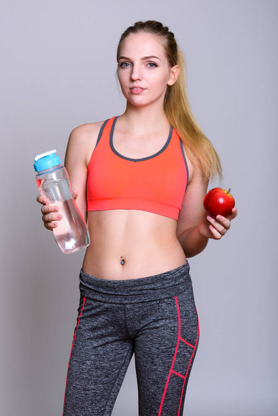 Young beautiful teenage girl holding water bottle and red apple  - Фото, зображення