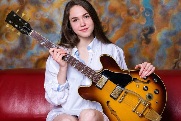 Young girl sitting on a red couch with electric guitar - Valokuva, kuva