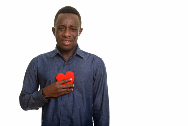 Young sad African man holding red heart on chest  - Photo, Image