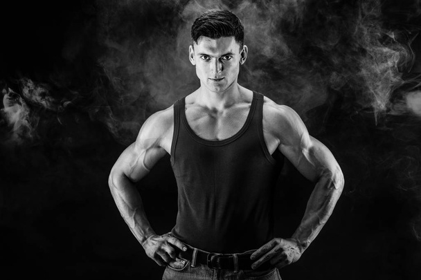 bodybuilder posing. Beautiful sporty guy male power. Fitness muscled man in shirt on dark smoky background - Foto, Imagem