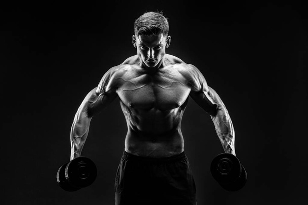 Handsome bodybuilder doing exercise with dumbbell. Studio shot. Black and white photo. - Foto, Imagem